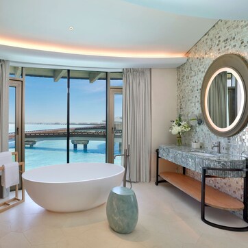 A modern bathroom with a large bathtub, two sinks, and a view of a bridge over water.