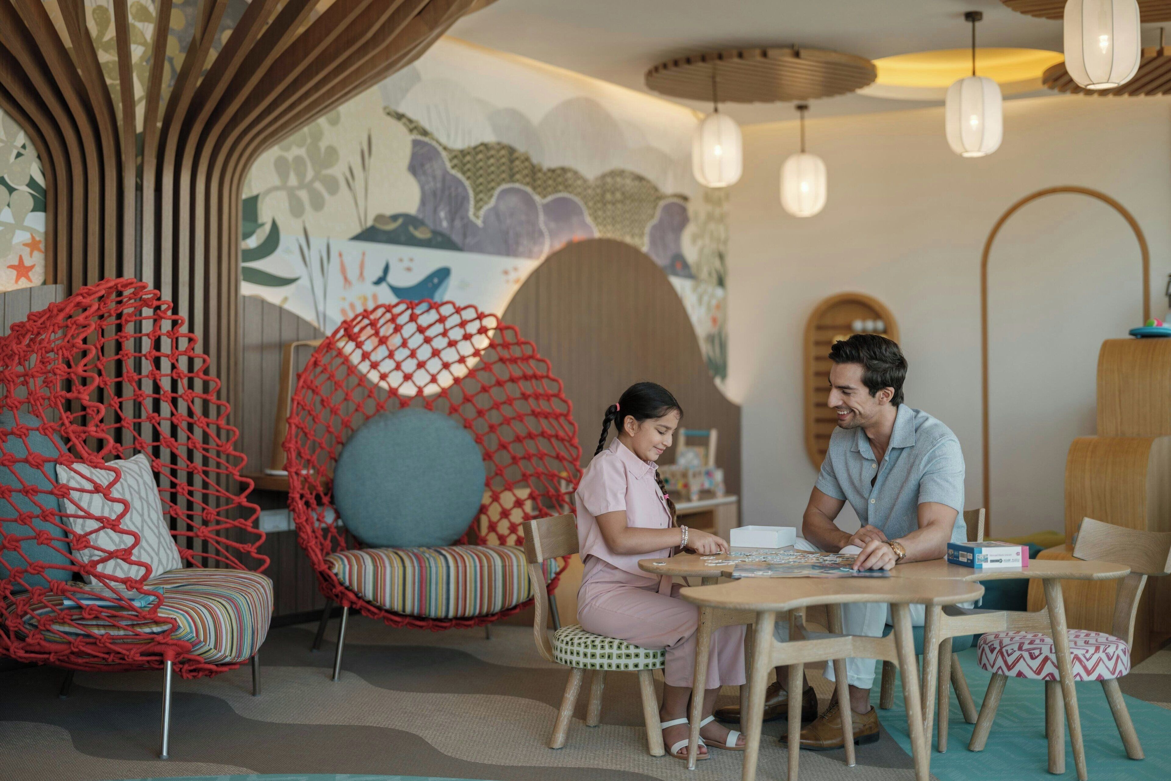 A cozy indoor setting with a wooden table, a red netted chair, and a mural on the wall.