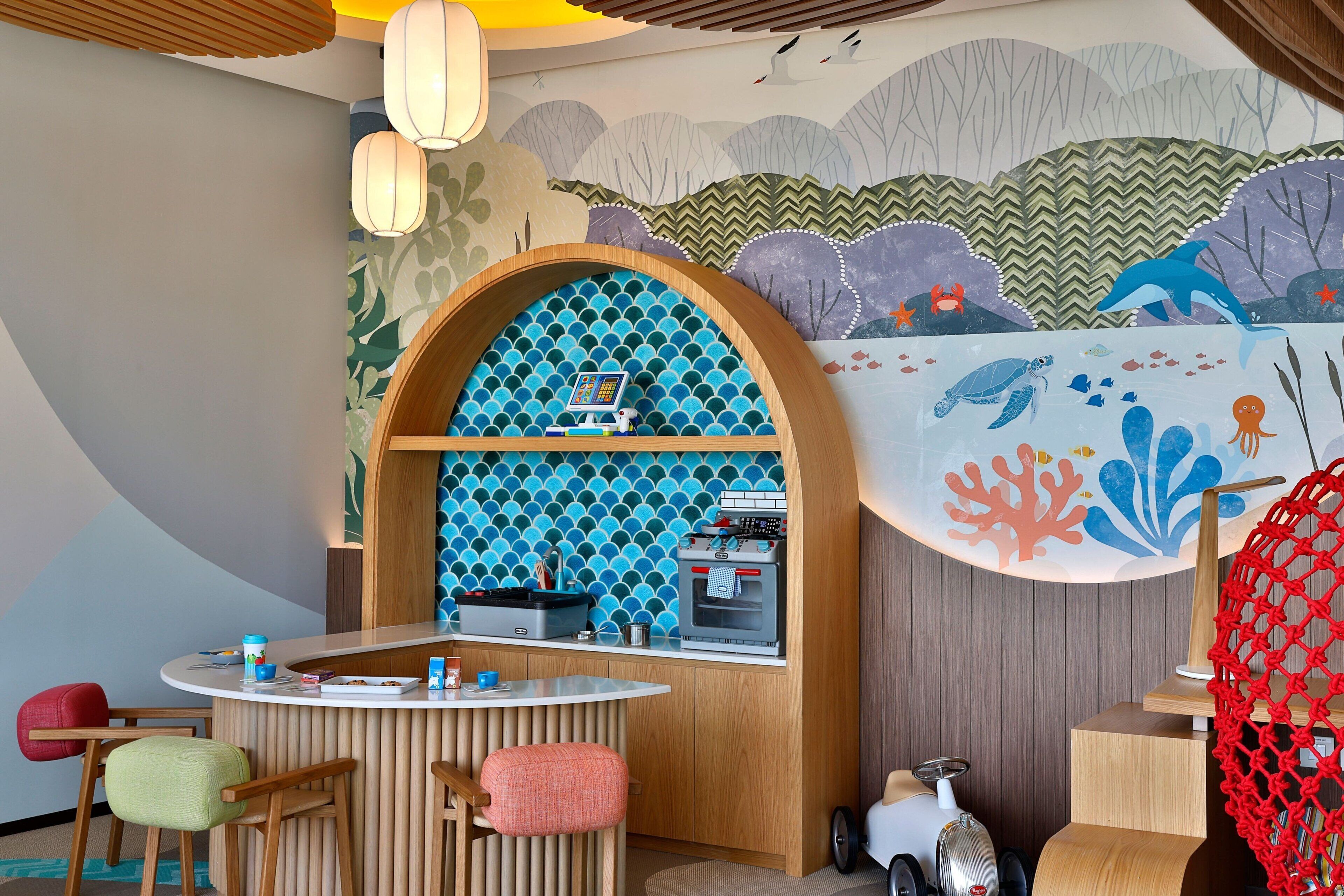 A children's play area with a wooden play kitchen, seating, and a mural of sea creatures.