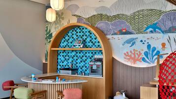 A children's play area with a wooden play kitchen, seating, and a mural of sea creatures.