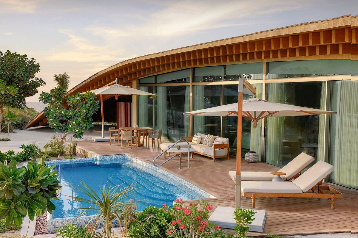 Un resort moderno con piscina, sillas de descanso y una terraza de madera.
