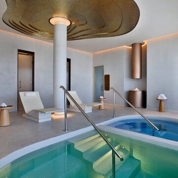 A modern indoor pool area with a clear pool, white lounge chairs, and a large column.
