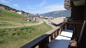 A view from a balcony overlooking a village with buildings, a grassy area, and mountains in the background. - Renovated studio at the foot of the slopes with balcony and equipped kitchen (La Plagne Montalbert)