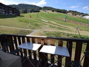 A deck with two white tables and chairs, overlooking a ski slope with buildings and a forested hill in the background. - Renovated studio at the foot of the slopes with balcony and equipped kitchen (La Plagne Montalbert)