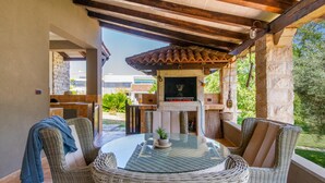 Un patio exterior con mobiliario de mimbre, una mesa de vidrio y una chimenea de piedra.