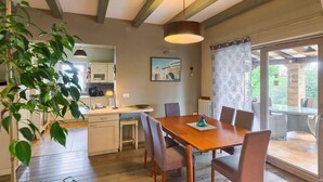 Un comedor con mesa y sillas de madera, una lámpara colgante y vistas al exterior a través de una puerta de cristal.