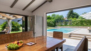 Un comedor con una mesa de madera, una cesta de frutas y vistas a una piscina y jardín.
