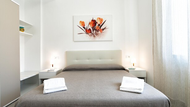 Une chambre d’hôtel moderne avec un grand lit, deux tables de chevet, une œuvre d’art accrochée au mur et une fenêtre avec des rideaux.