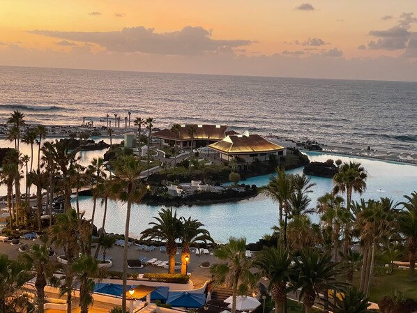 Un complexe hôtelier doté d’une piscine, de palmiers et offrant une vue sur l’océan au coucher du soleil.