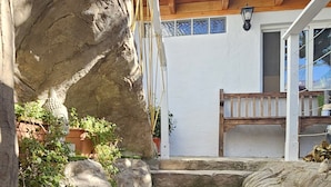 A stone staircase leading up to a wooden deck with a white exterior wall and windows.