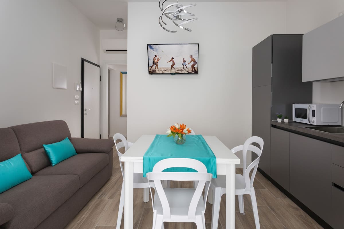 A modern living room with a brown sofa, white chairs, a teal tablecloth, and a painting above the table.