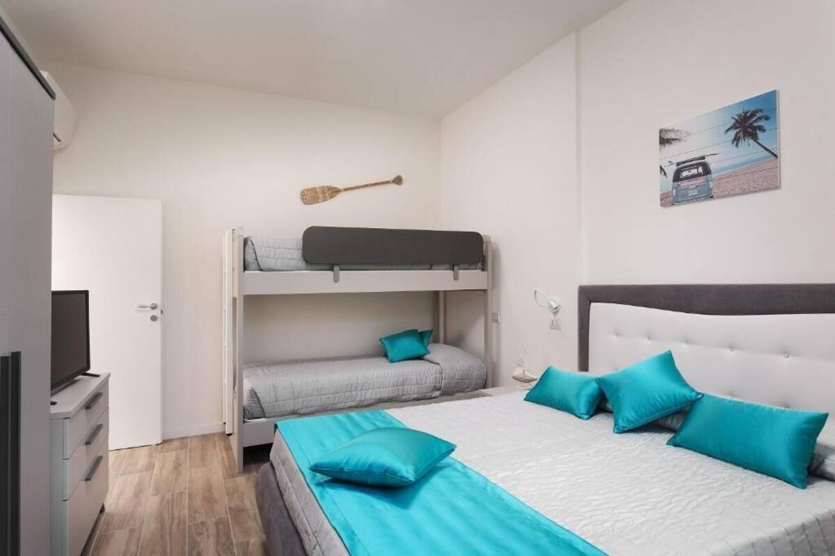 A bedroom with bunk beds, a bed with pillows, a television, and a painting on the wall.
