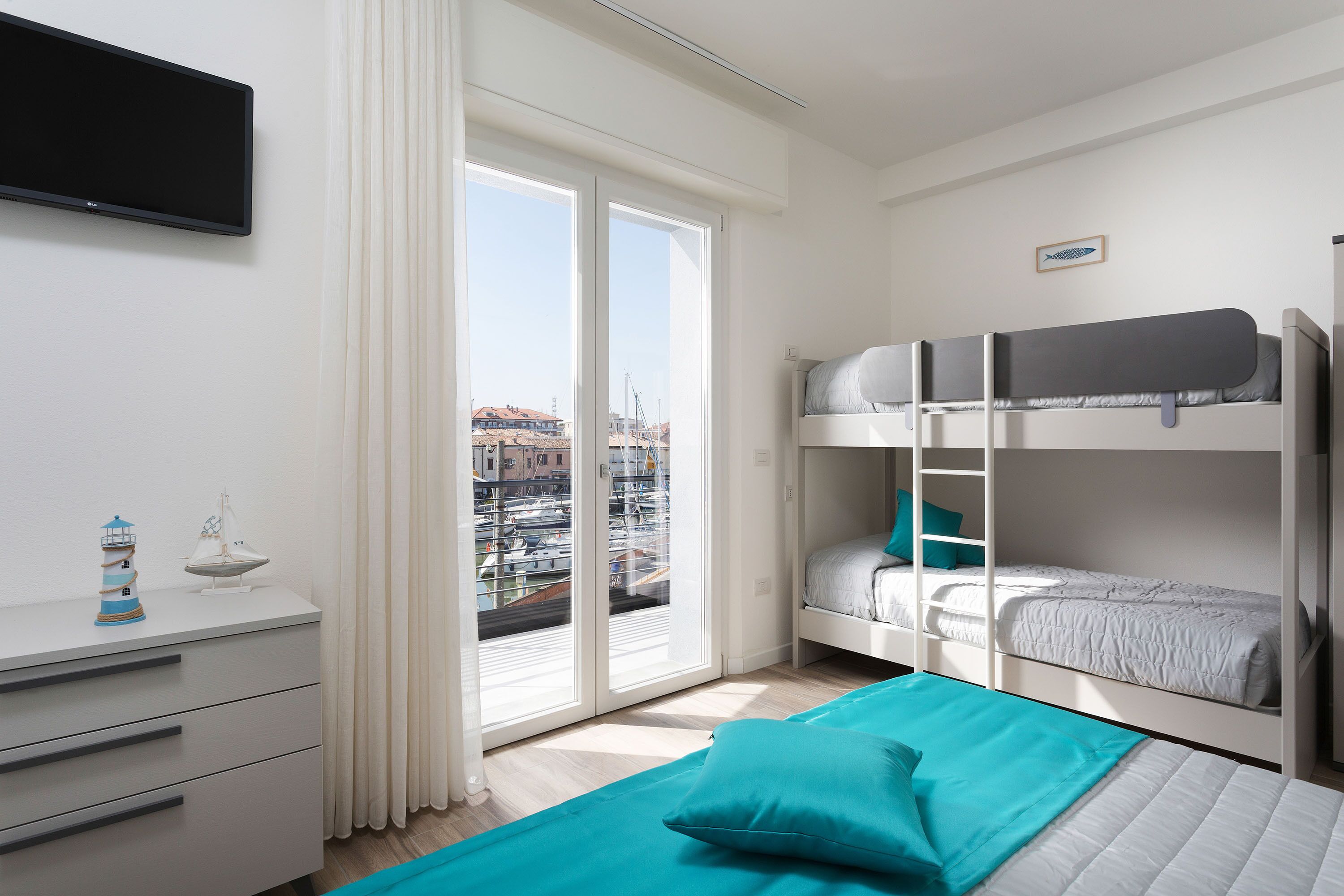 A modern hotel room with a balcony, a TV, a dresser, and bunk beds.