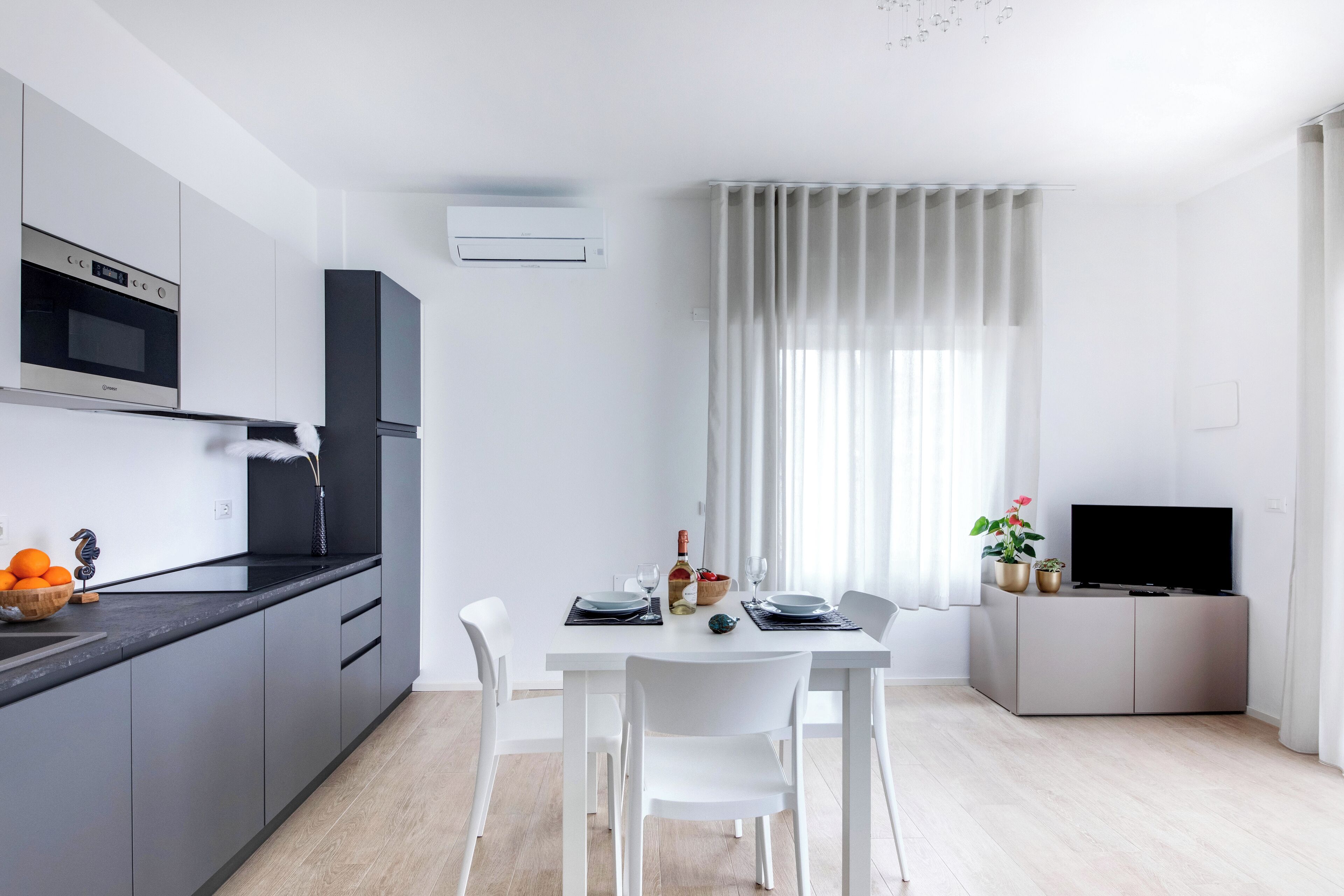 A modern kitchen with a built-in oven and microwave, a dining area with a table set for four, and a flat-screen TV on a cabinet.