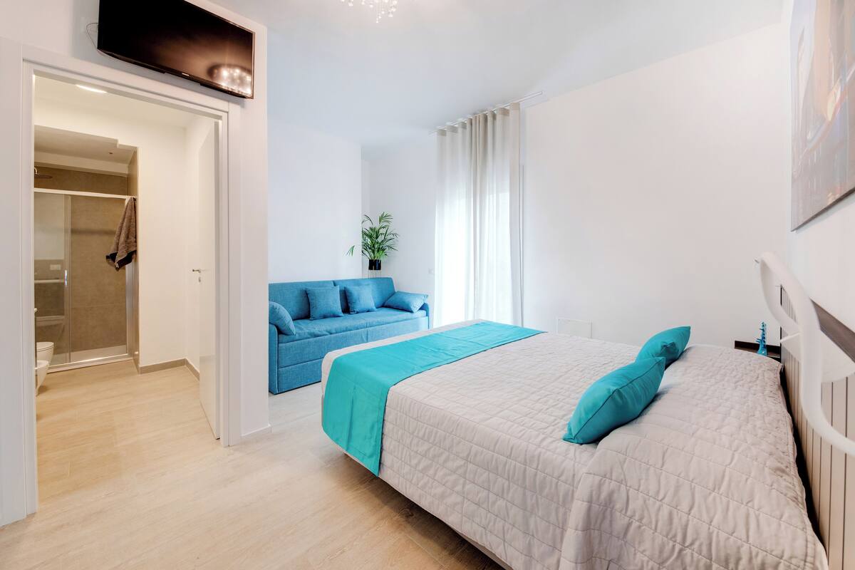 A modern bedroom with a large bed, a blue sofa, and a shower area.
