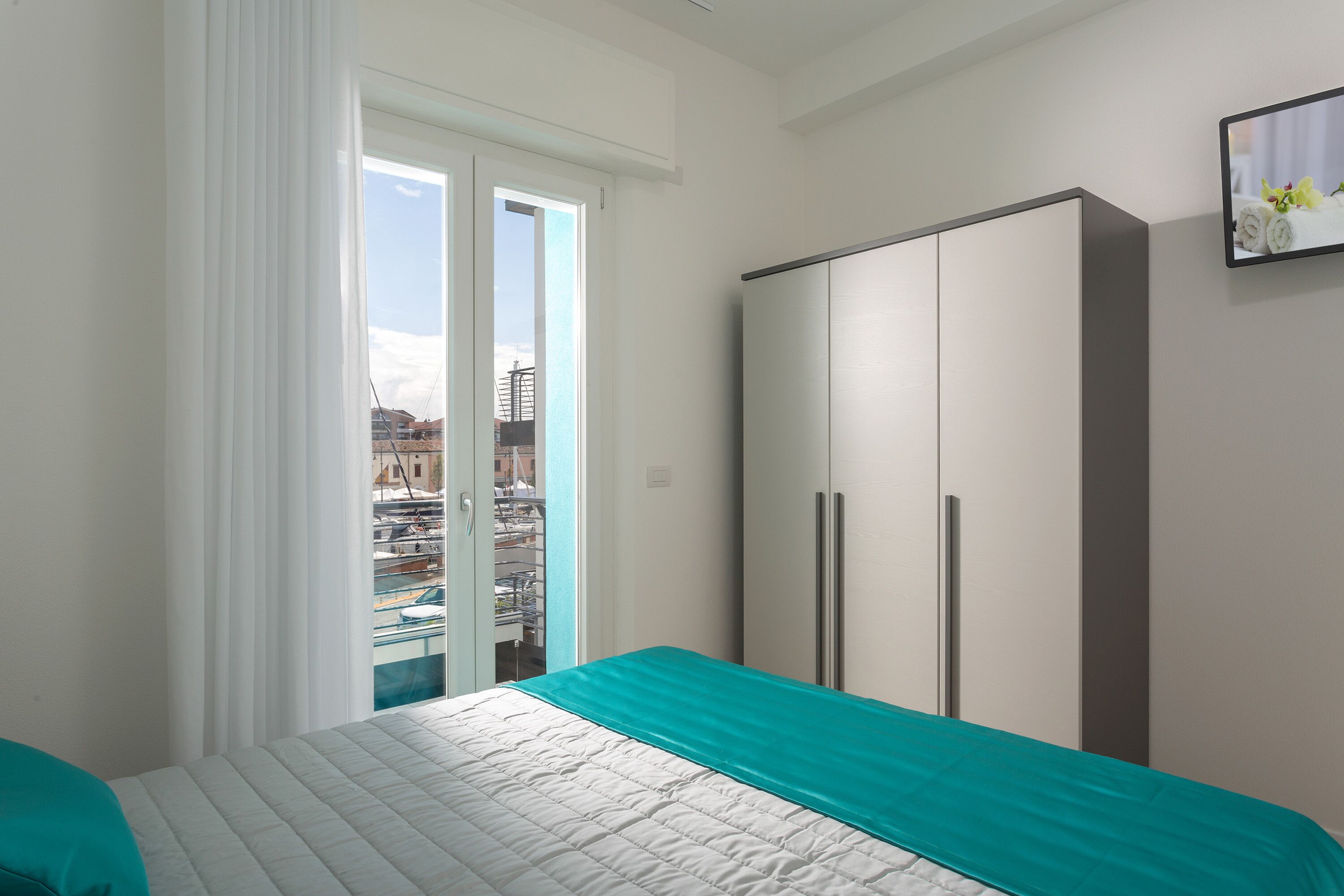 A bedroom with a bed, a wardrobe, a sliding glass door to a balcony, and a framed picture on the wall.