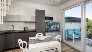 Una cocina moderna con comedor, televisor y balcón con sillas azules.