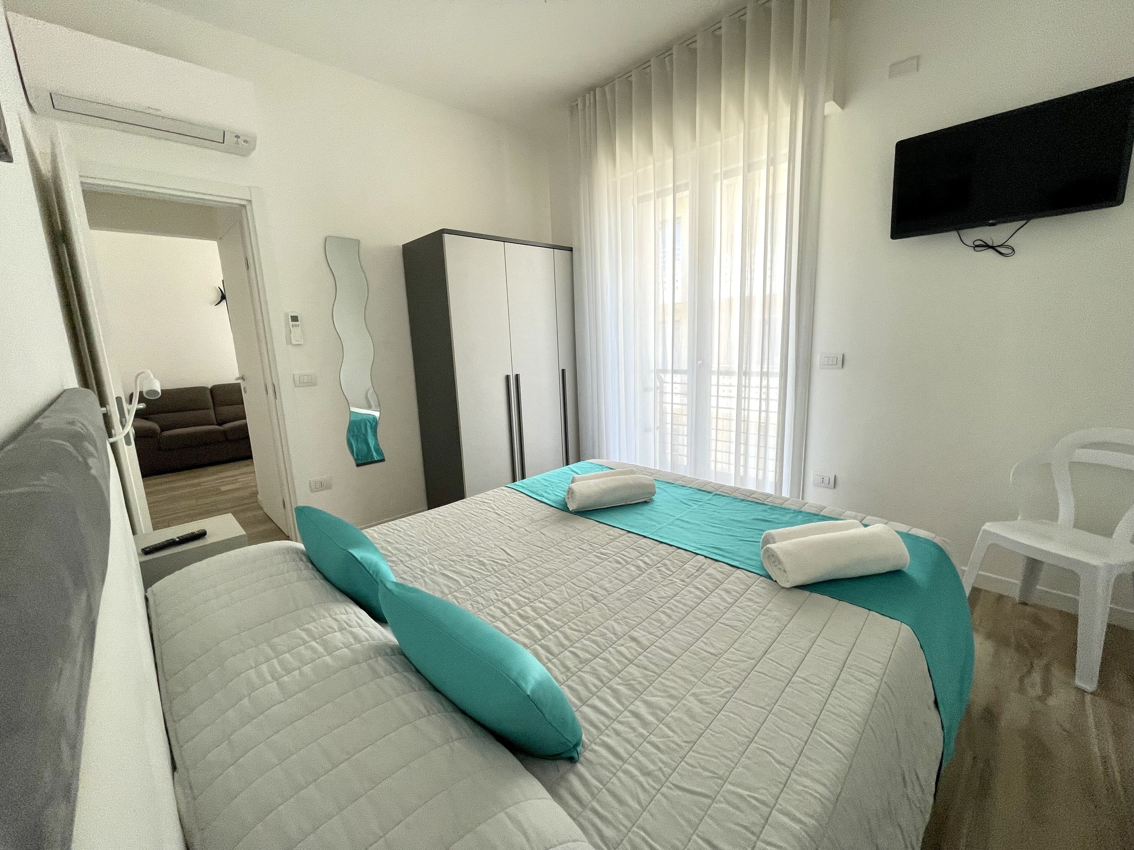 Ein Hotelzimmer mit einem Bett, einem an der Wand befestigten Fernseher, einem Kleiderschrank und einem Fenster mit Vorhängen.