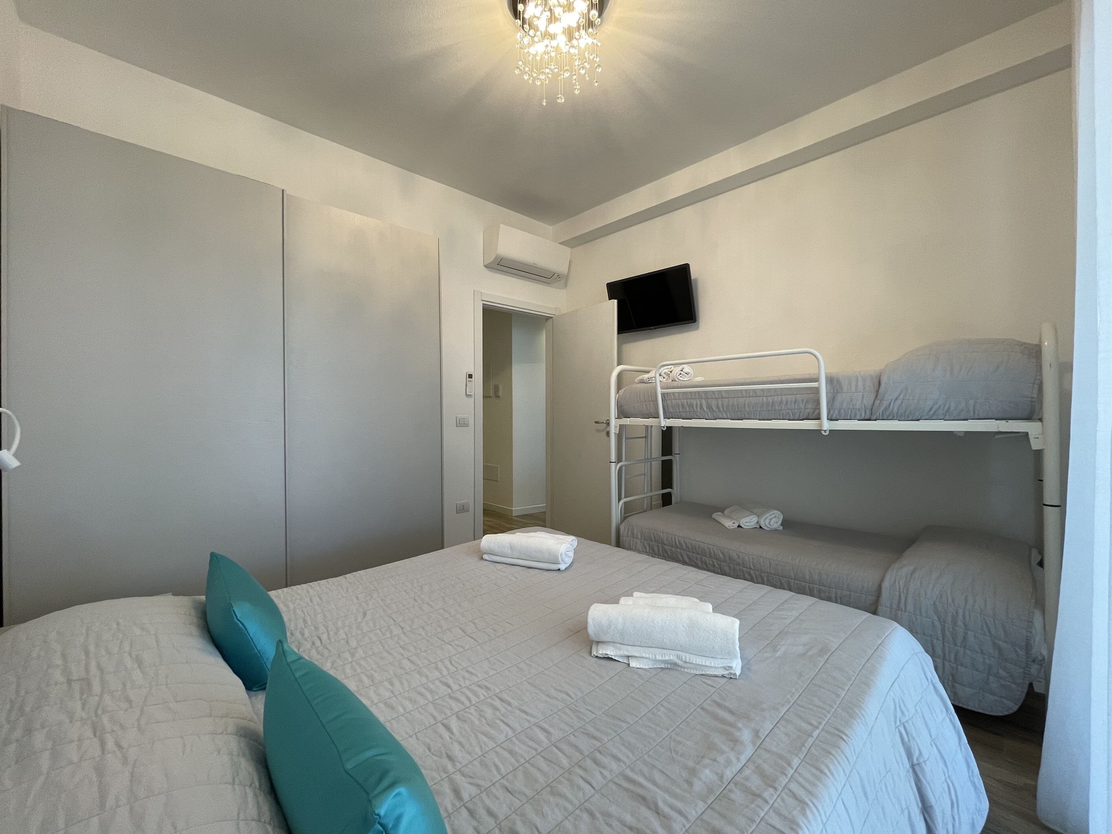 Ein Schlafzimmer mit einem Etagenbett, einem Einzelbett mit einem türkisfarbenen Kopfkissen und einem an der Wand montierten Fernseher.