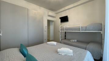 Ein Schlafzimmer mit einem Etagenbett, einem Einzelbett mit einem türkisfarbenen Kopfkissen und einem an der Wand montierten Fernseher.
