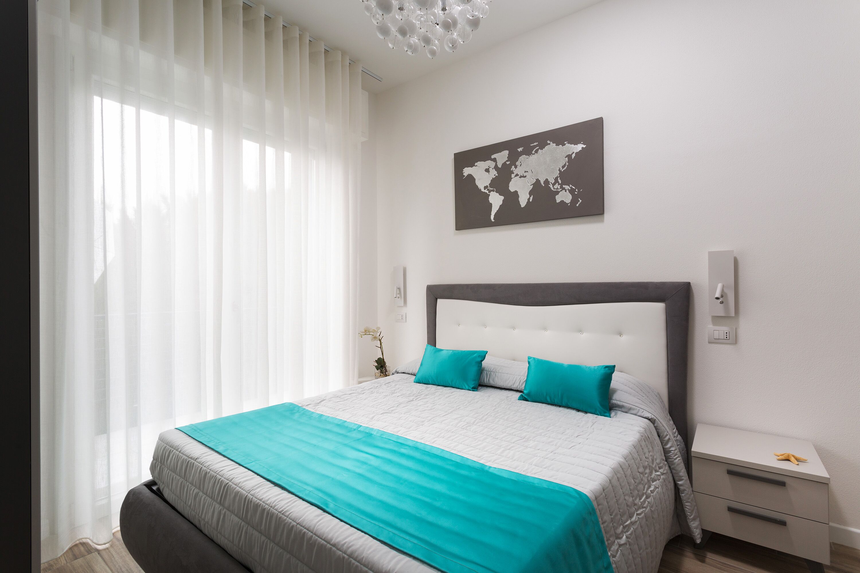 A modern bedroom with a large bed, a world map on the wall, and a bedside table with a lamp.