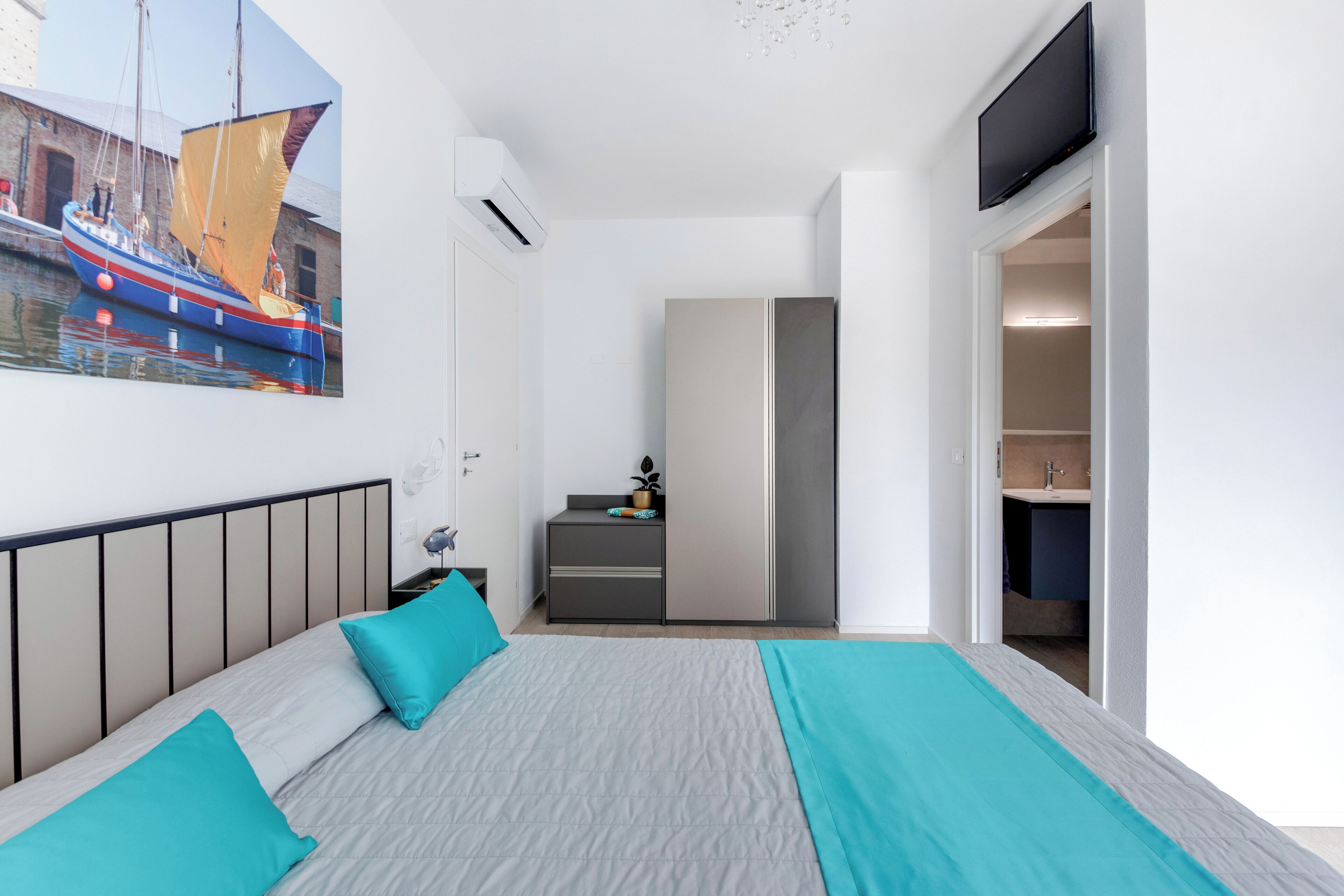 Een slaapkamer met een bed, een bureau, een stoel, een televisie en een badkamer zichtbaar door een geopende deur.