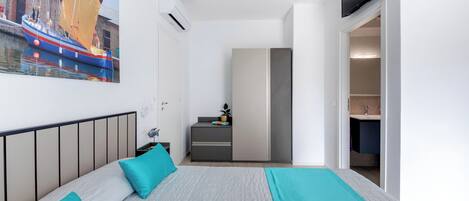 A bedroom with a bed, a desk, a chair, a TV, and a bathroom visible through an open door.