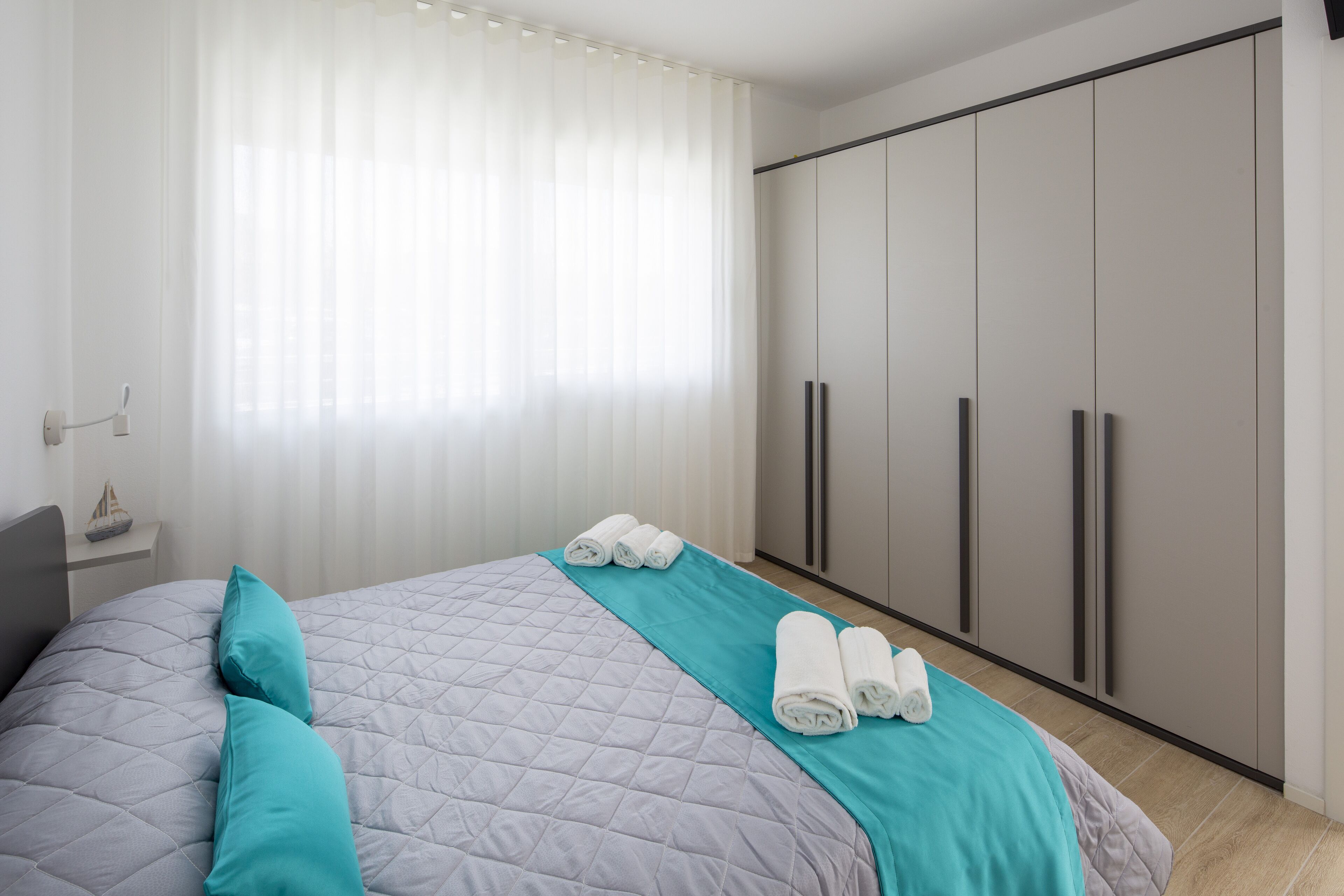 A hotel room with a bed, a nightstand, a large wardrobe, and a window with sheer curtains.