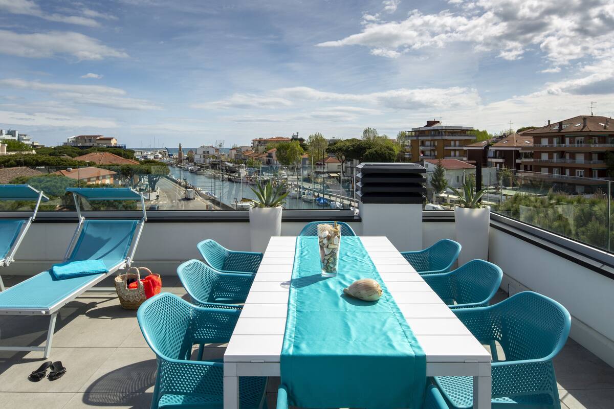 A rooftop terrace with a table and chairs, a view of the marina, and buildings in the background.