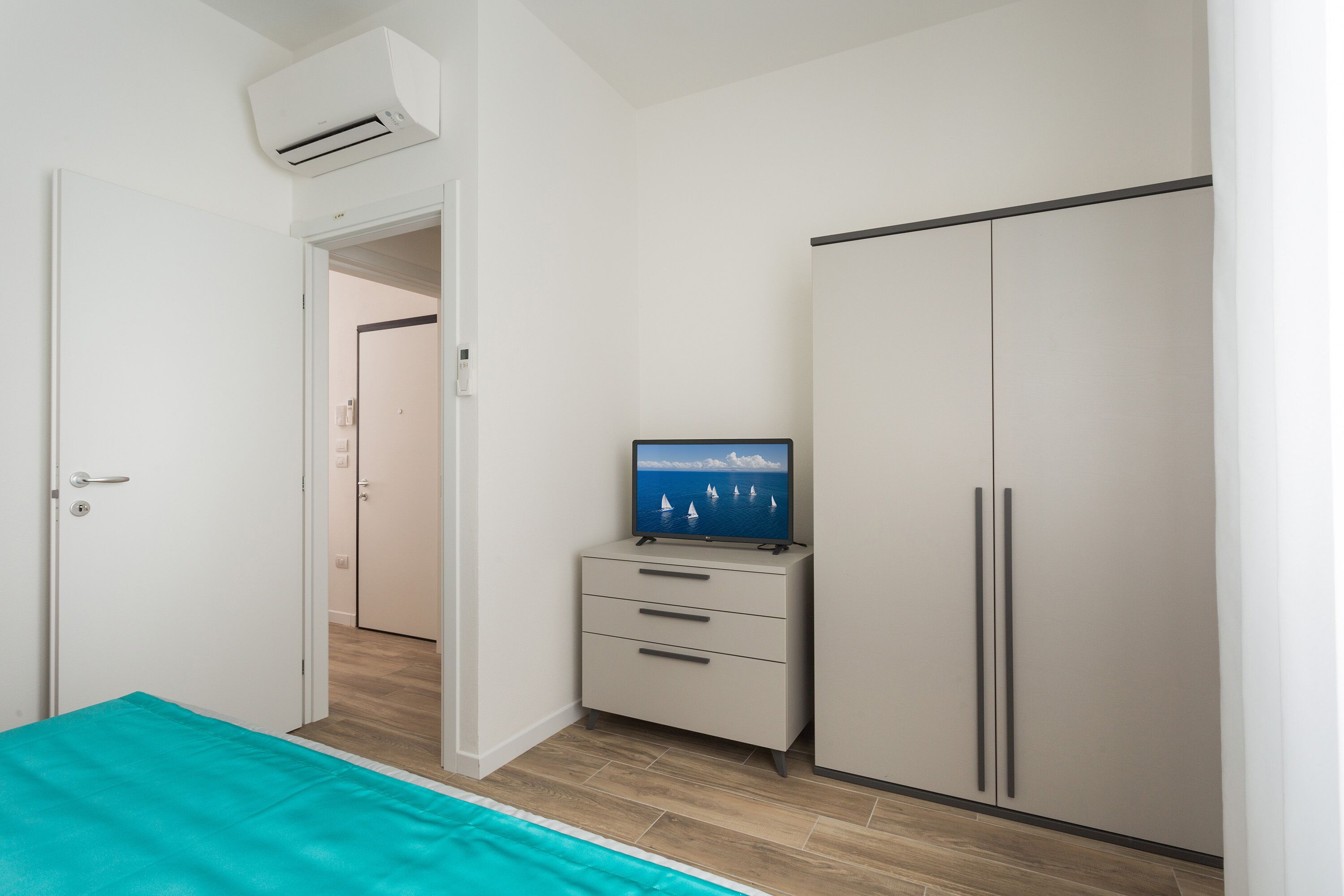 Une chambre à coucher avec un lit, un téléviseur posé sur une commode, une armoire et un appareil de climatisation.
