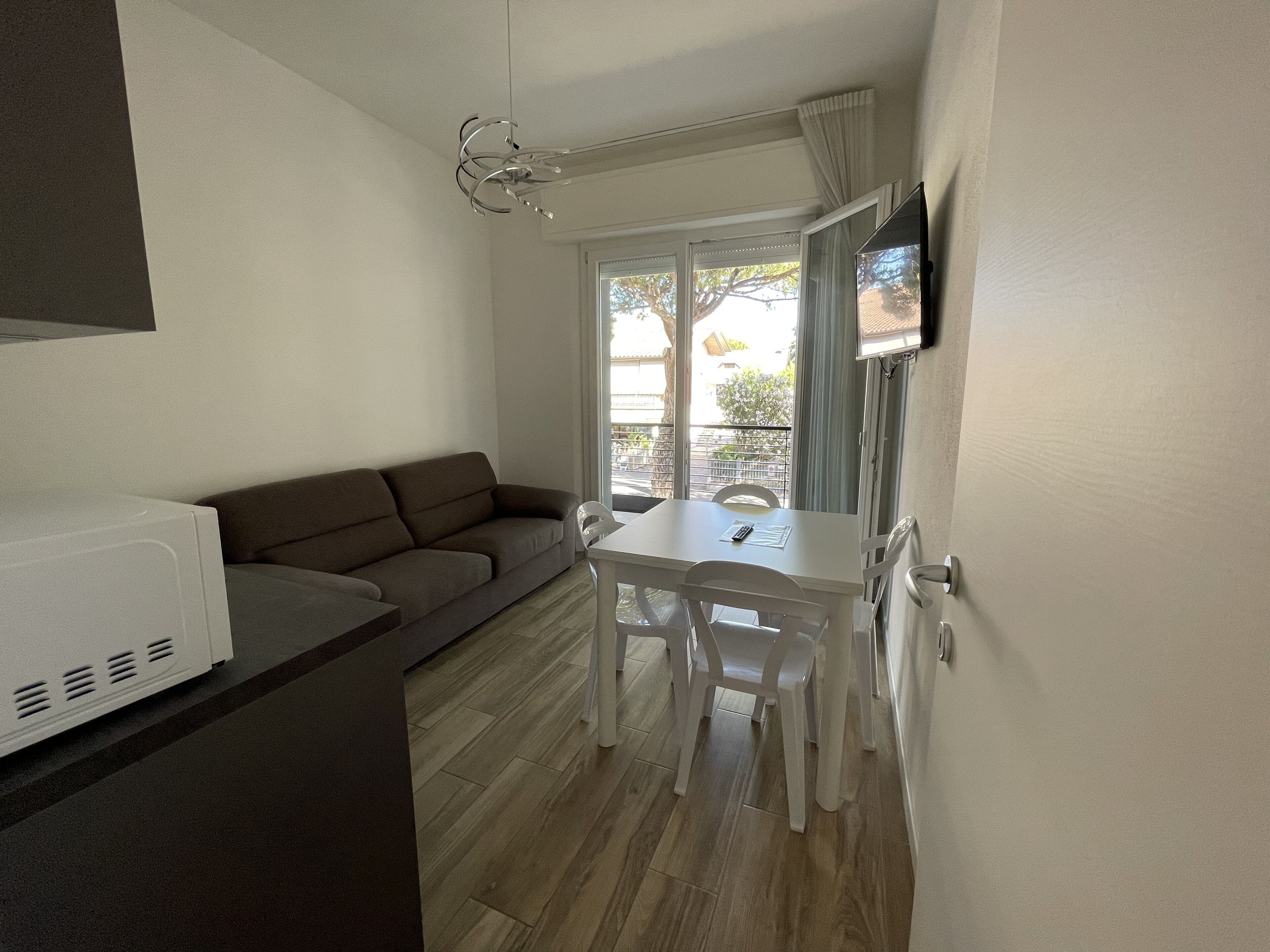 A compact living space with a sofa, a dining table with chairs, a TV mounted on the wall, and a sliding glass door leading to an outdoor area.
