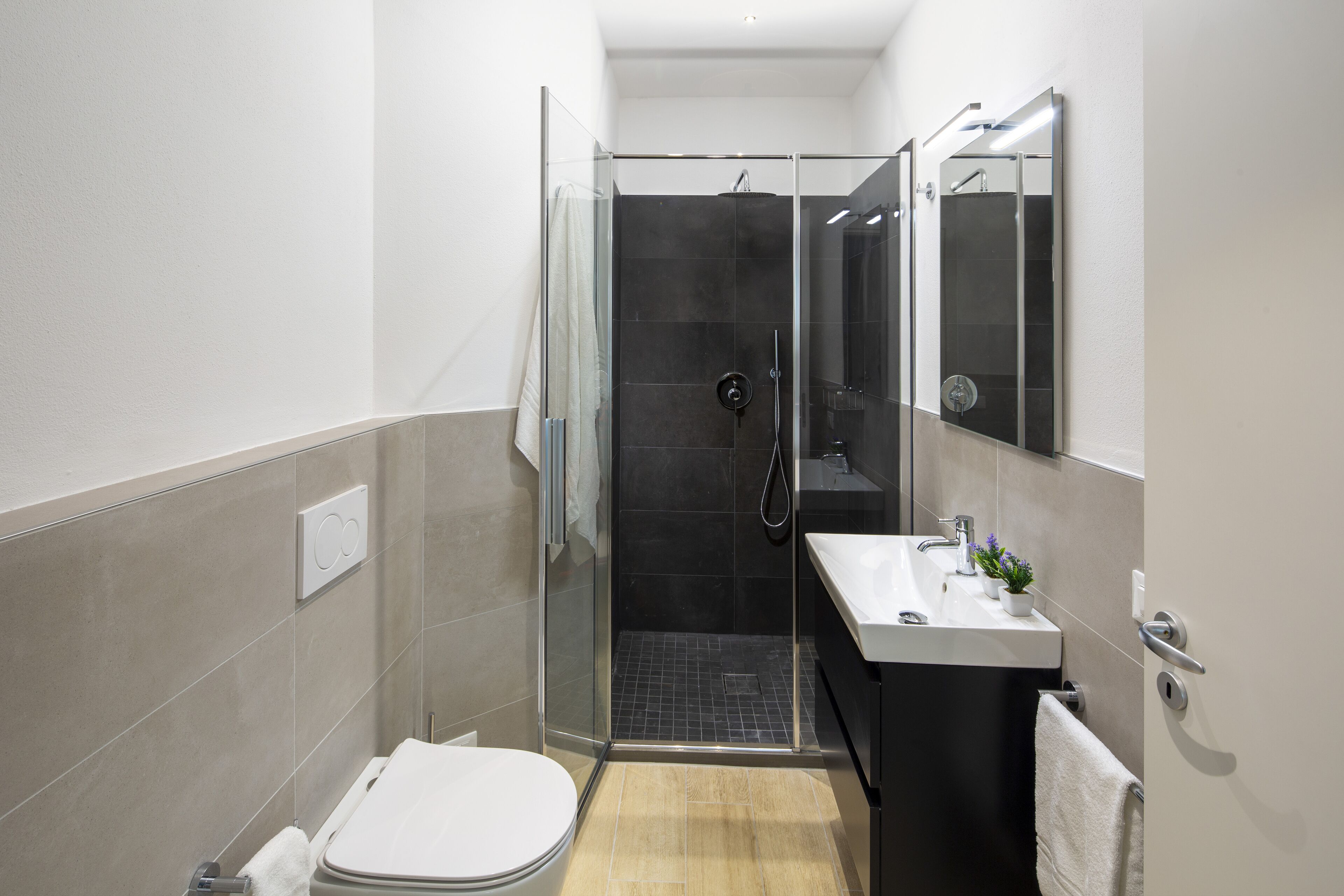 Un baño moderno con ducha envuelta en vidrio, inodoro blanco y lavamanos con espejo.