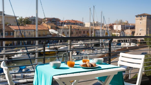 Una mesa con alimentos para el desayuno y vistas a un puerto deportivo con barcos y edificios.
