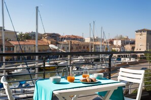 Una mesa con alimentos para el desayuno y vistas a un puerto deportivo con barcos y edificios.