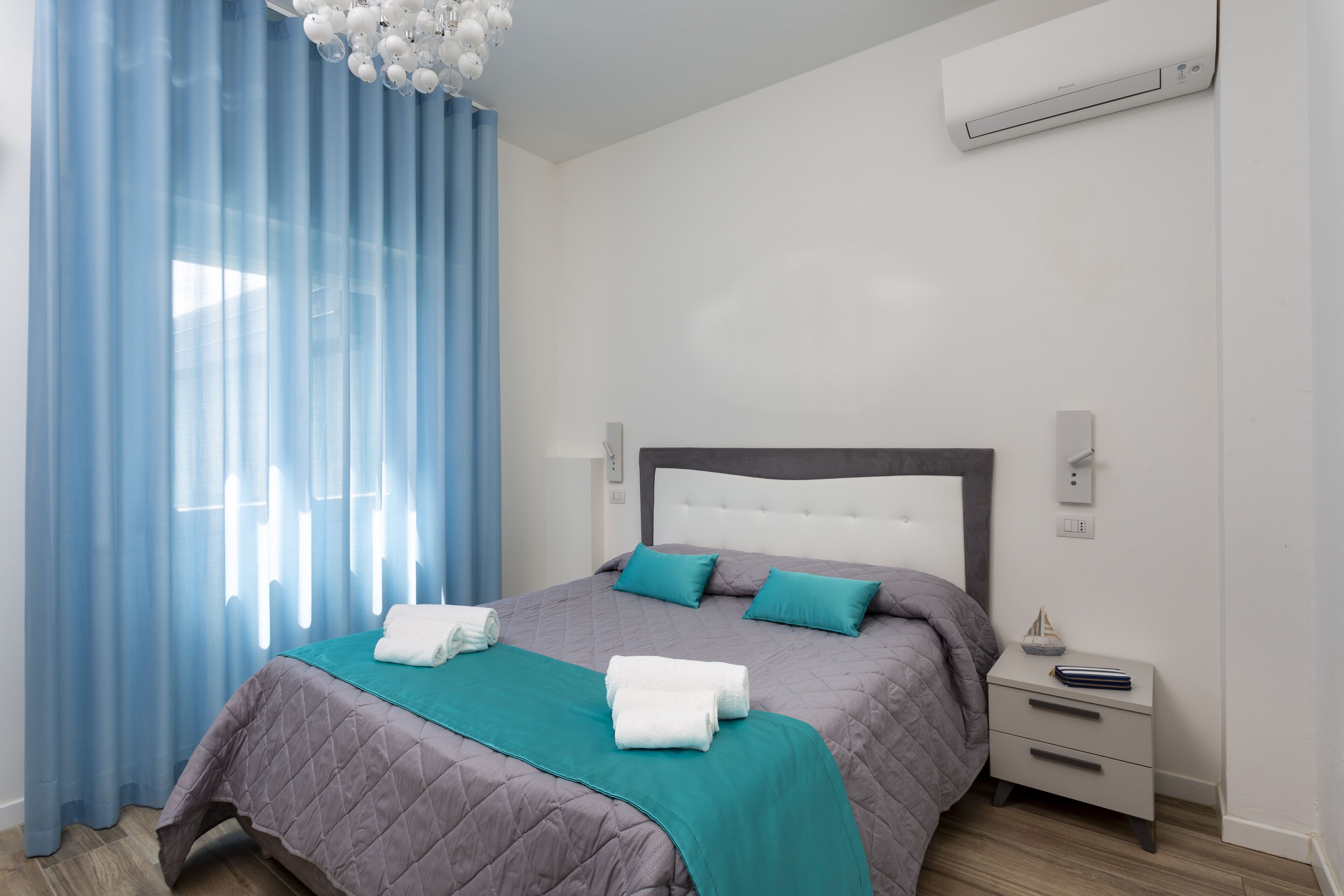 A modern bedroom with a large bed, a nightstand, and a wall-mounted air conditioner.
