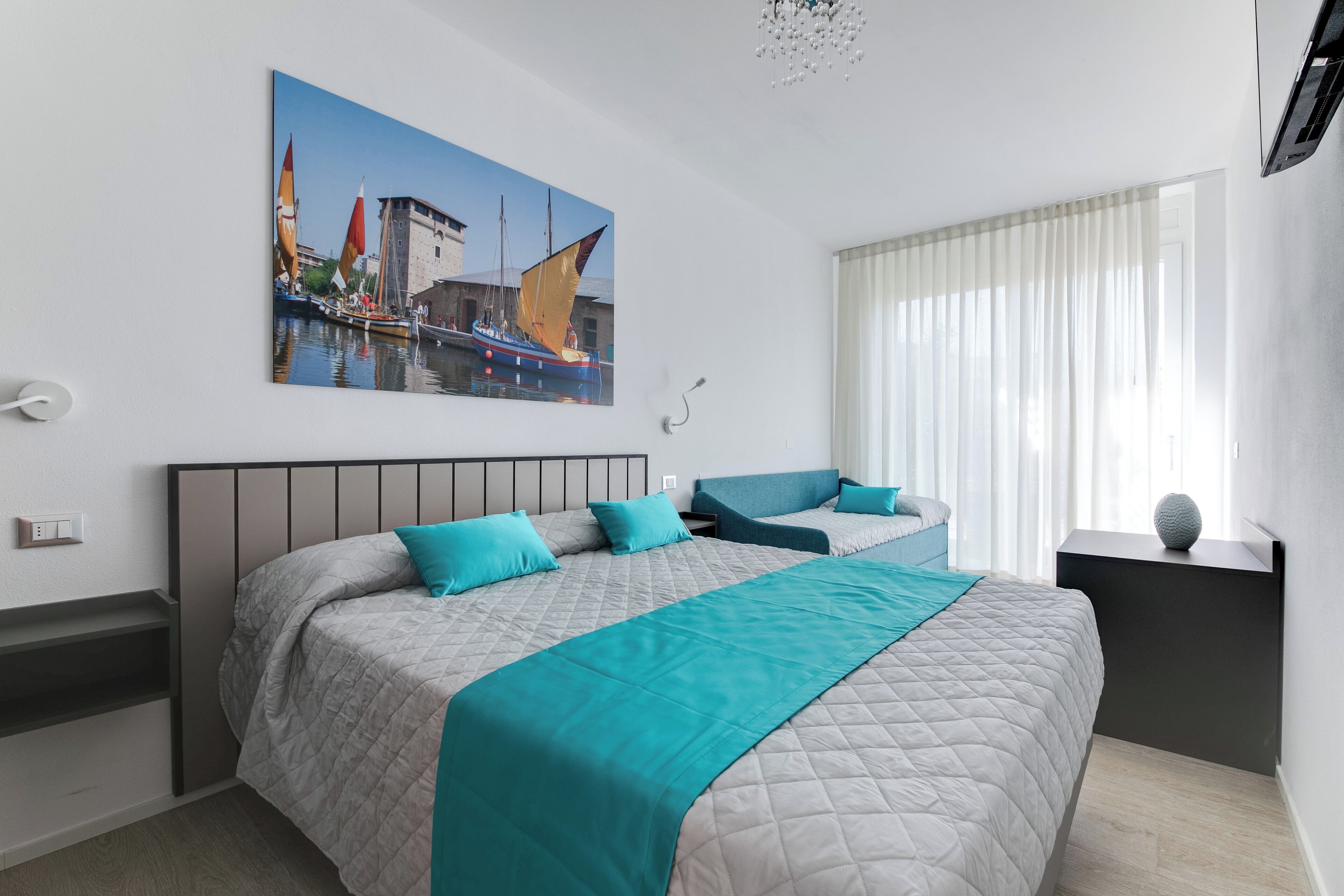 Una habitación de hotel moderna con una cama grande, dos mesitas de noche, un cuadro de un paisaje urbano y una ventana con cortinas.