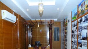 A room with a wooden wall, a yellow sofa, two wooden chairs, a desk, and a large poster on the wall. - Finix Residency (Puducherry)