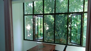 A room with a table and a chair, large windows with a view of greenery outside. - Finix Residency (Puducherry)