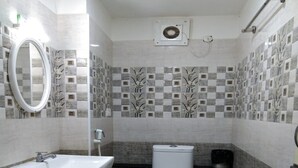 A compact bathroom with a white sink, toilet, and shower. The walls are tiled with a checkered pattern and a floral design. - Finix Residency (Puducherry)