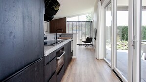 A modern kitchen with dark cabinetry, a granite countertop, and a built-in oven. There is a dining area with a black chair and a small table. The room has large windows with blinds, and a sliding glass door leads to an outdoor area. - 2 bedroom nice home in Voorthuizen (Voorthuizen)