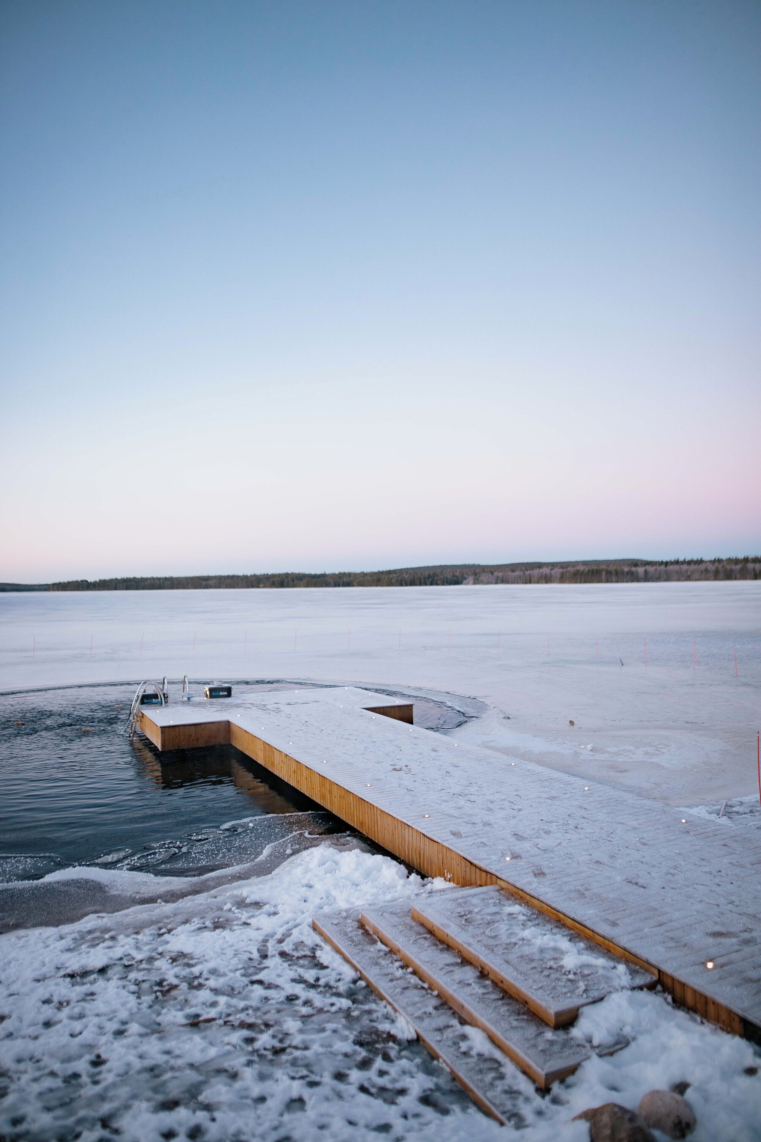 A wooden dock extending into a frozen lake with a clear sky.