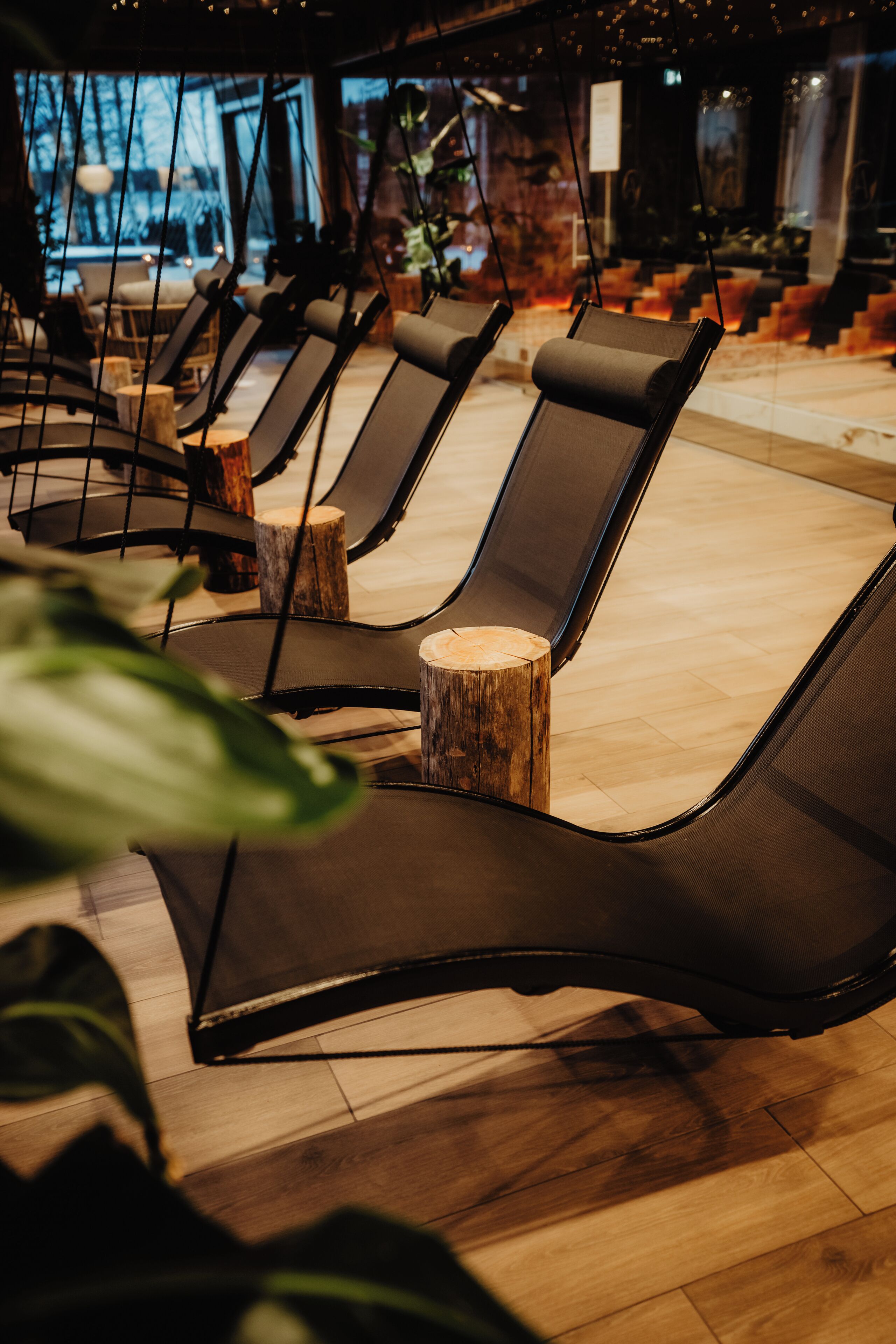 A row of lounge chairs with wooden stumps as bases, arranged in a modern indoor setting with wooden flooring and a view of the outdoors.