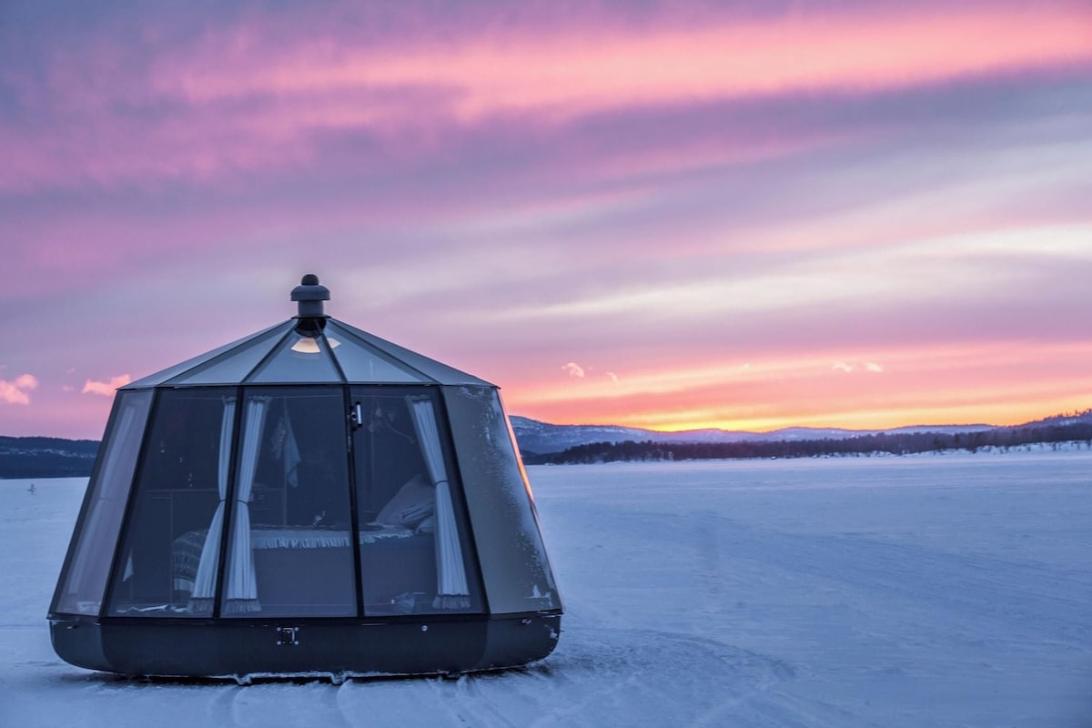 A geodesic dome structure on a frozen lake with a sunset in the background.