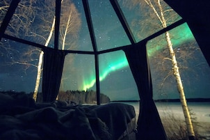 Una habitación con un ventanal grande, una cama y vistas de las auroras boreales.