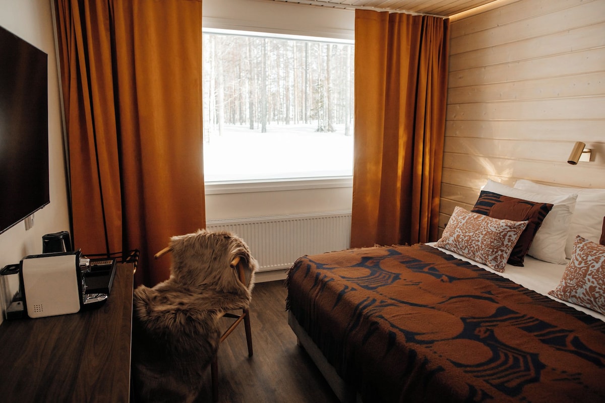 A hotel room with a bed, a chair, a TV, and a window with curtains.