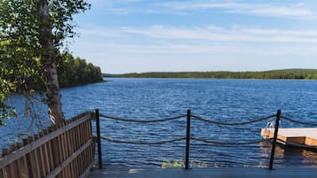 A person relaxing in a hot tub on a wooden deck by a lake.