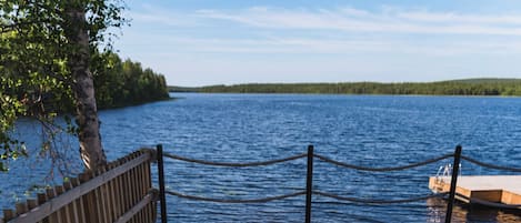 A person relaxing in a hot tub on a wooden deck by a lake.