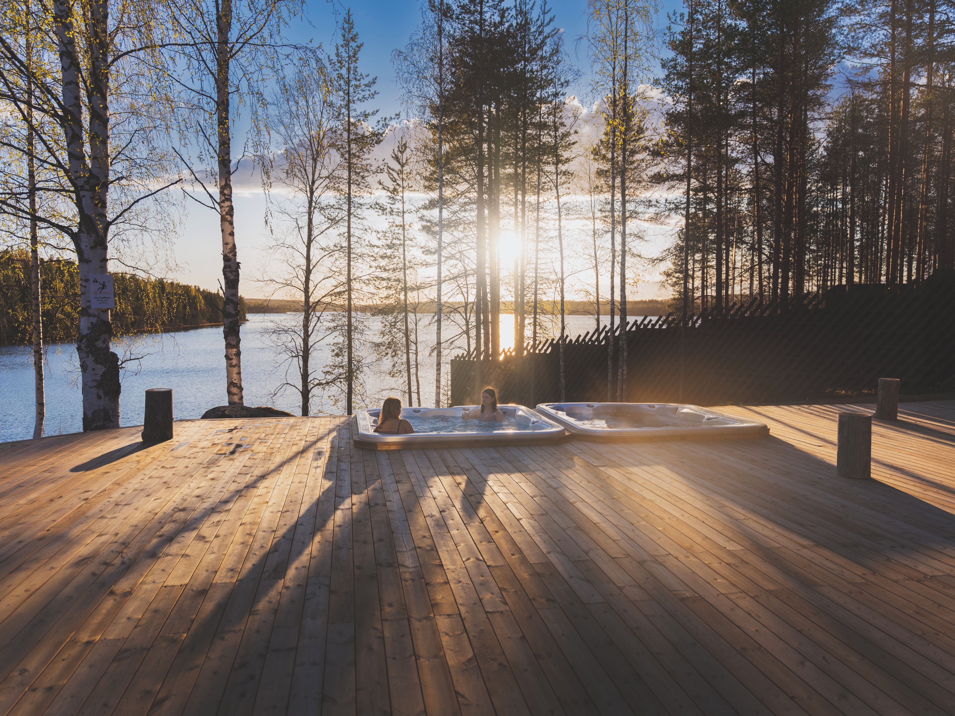 Una terraza de madera con jacuzzis y vista al lago.