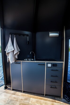 A compact kitchenette with a sink, a small window, and a towel hanging on the wall.