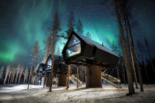 Zona exterior cubierta de nieve con una estructura de edificio moderna, con ventanas amplias y una escalera que sube a una plataforma.